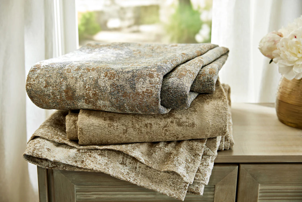 Stack of folded textured coverlets on a wooden surface with a blurred natural background