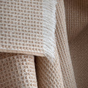A close-up of a textured waffle-weave throw blanket in a beige colour, featuring fringed edges.