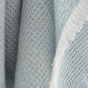 A close-up of a textured waffle-weave throw blanket in a baby blue colour, featuring fringed edges.
