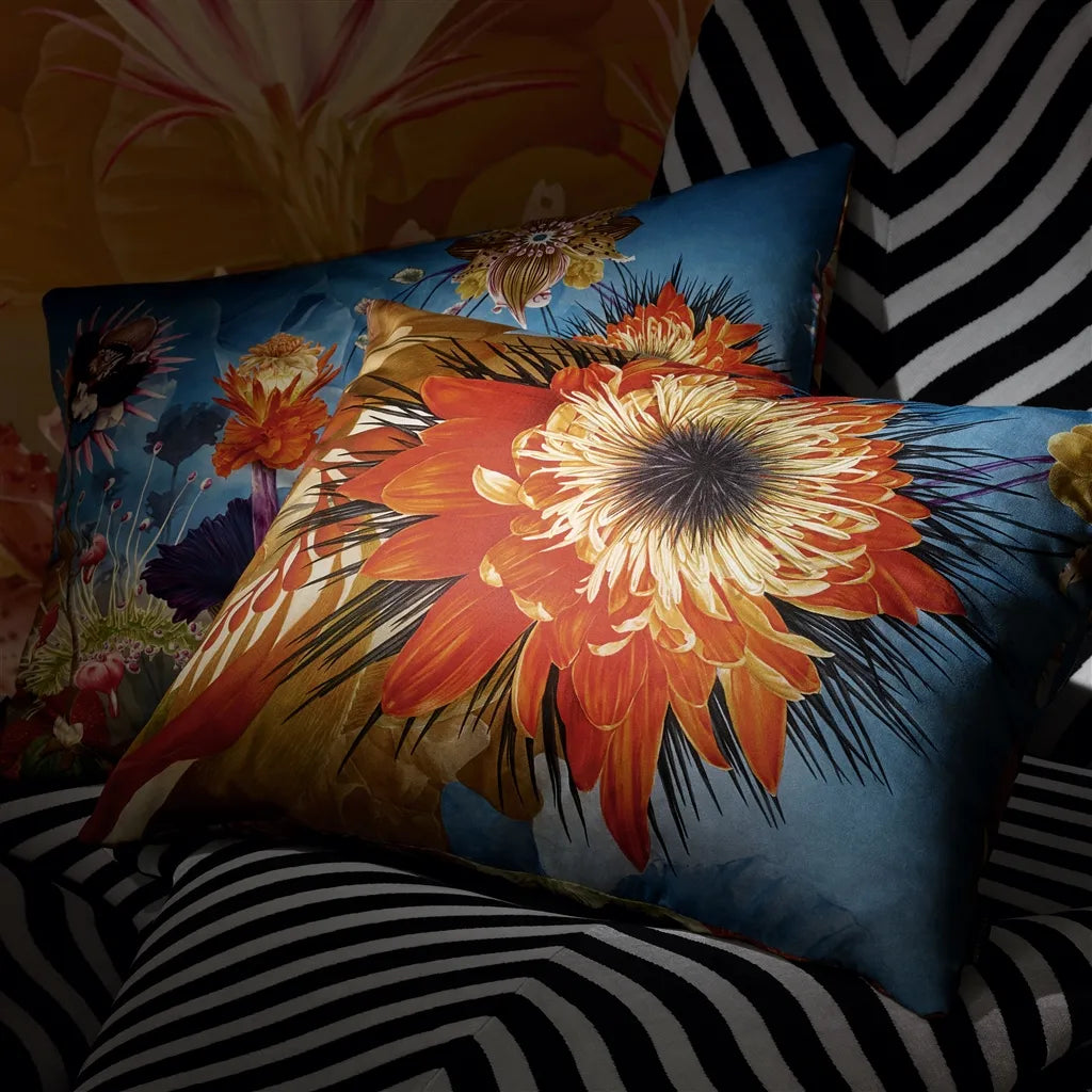Surrearles'isme - Mosaique Decorative Pillow has a vibrant floral design, predominantly featuring orange and yellow flowers on a blue background, placed on a bed with a striped cover.