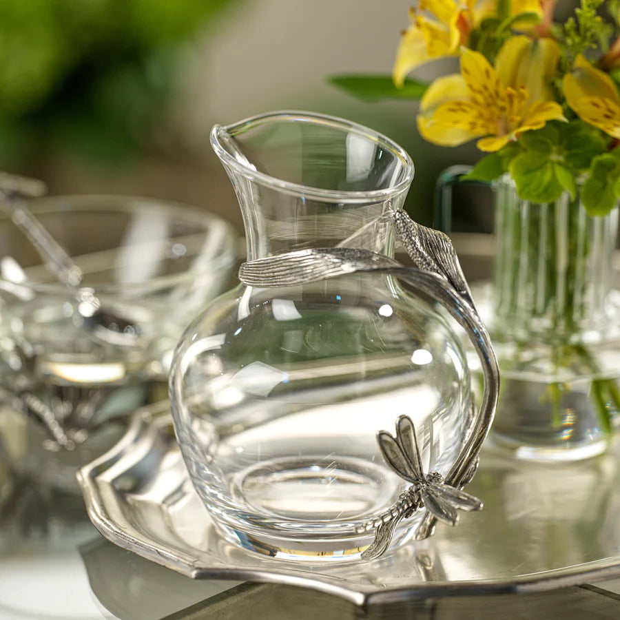 Dragonfly pewter and glass carafe shown on tray with vase with flowers in background on right