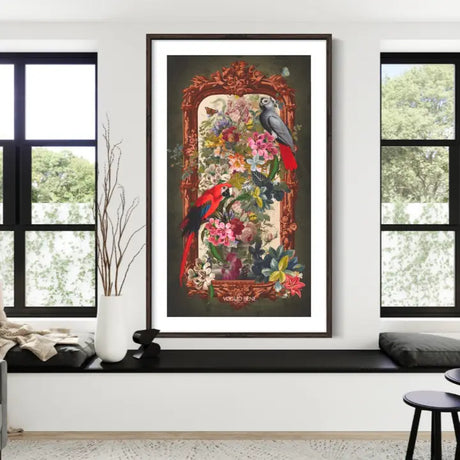 A framed vertical wall hanging featuring two red and green parrots among a dense floral arrangement, displayed on a white wall above a black bench in a modern room setting.