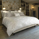 Bedroom with a bed featuring a silver grey leafty patterned duvet, bookshelves, and a stone wall.