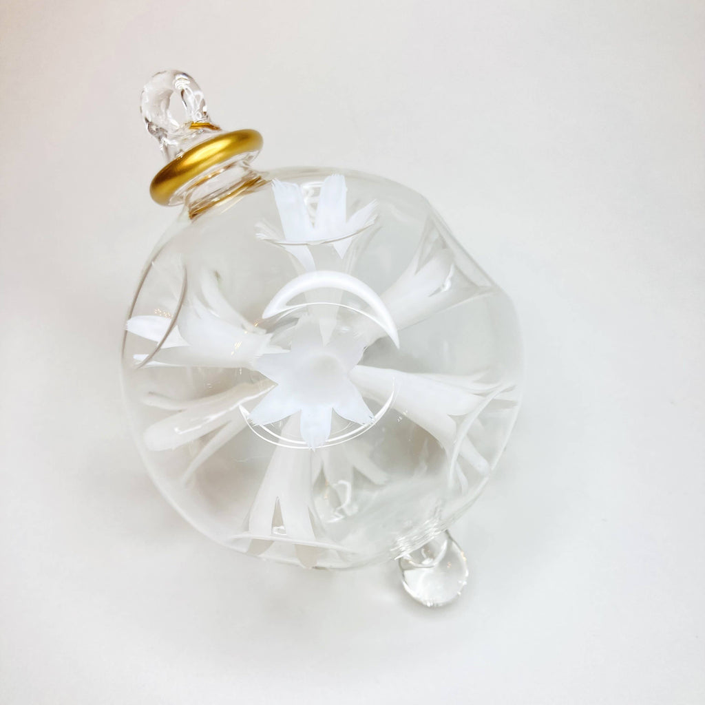Clear glass ornament with a white flowers and gold accent on a white background