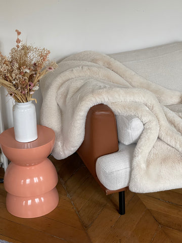 Cream Faux Fur throw shown draped on couch with dried flowers in vase on sculptured side table to the left