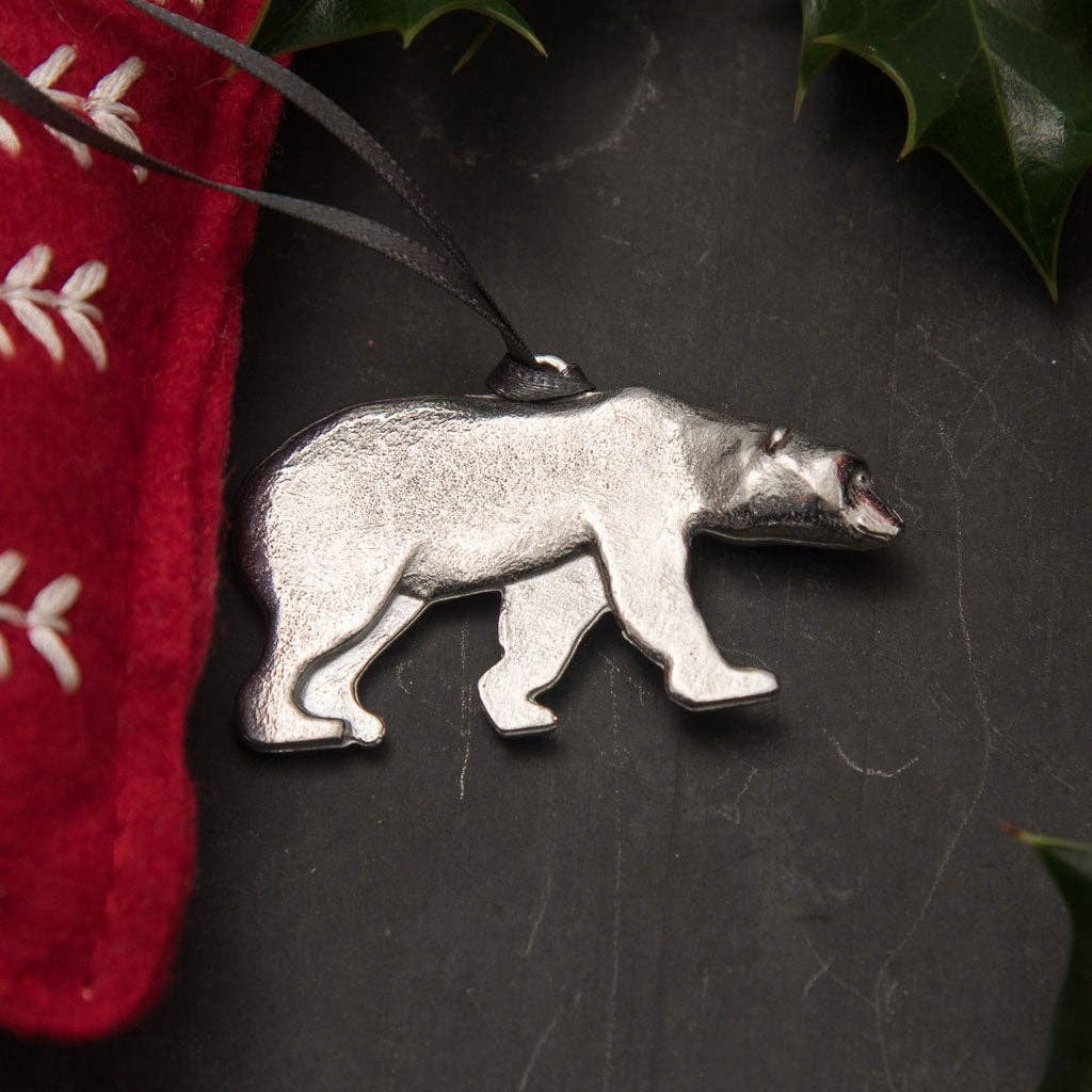 Pewter bear ornament on a dark surface with a red fabric and green leaves in the background
