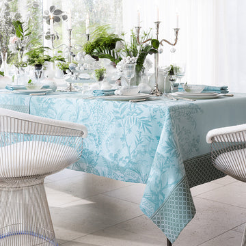 Jardin D'Eden Blue Tablecloth with tone on tone delicate botanical details woven in aqua tones. Draped on table with contemporary yet formal table setting with crystal glasses and a plethora of white accents.