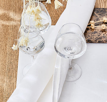 Marie-Galante White napkin with subtle tone on tone white flower pattern folded between glasses with water.