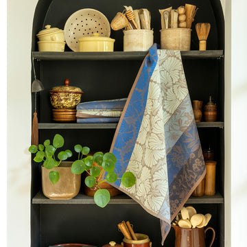 Cottage Blue tea towel shown hanging from a set of shelves filled with various kitchen utensils and a plant