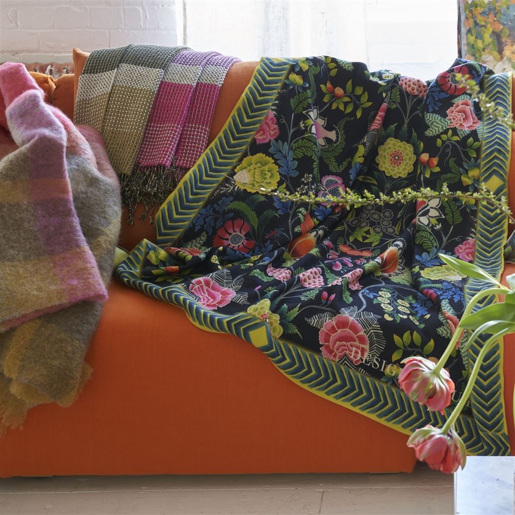 Brocart Decoratif Throw Noir shown draped on right side of orange couch with flowers in foreground and two other throws draped on left side of couch
