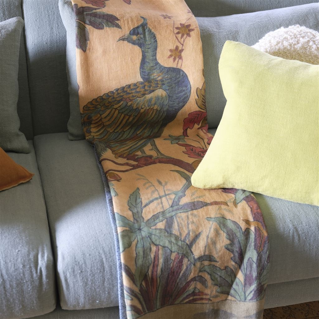Peacock Toile Sepia Throw shown folded on blue couch with the edges of pillows on either side, overlapping on right side